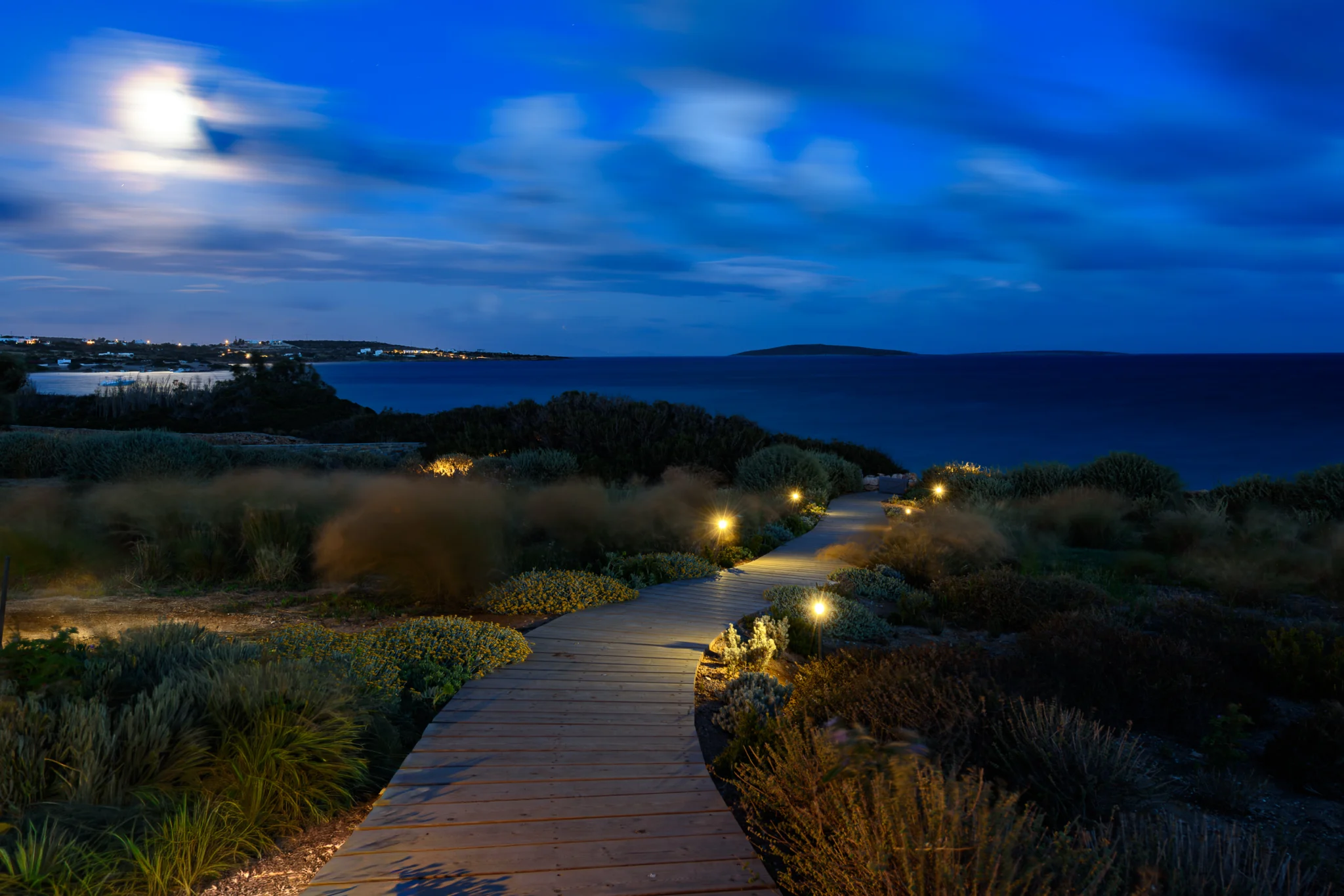 Garden boardwalk with low path lights leading towards the sea at night at Villa Seafront, Paros.