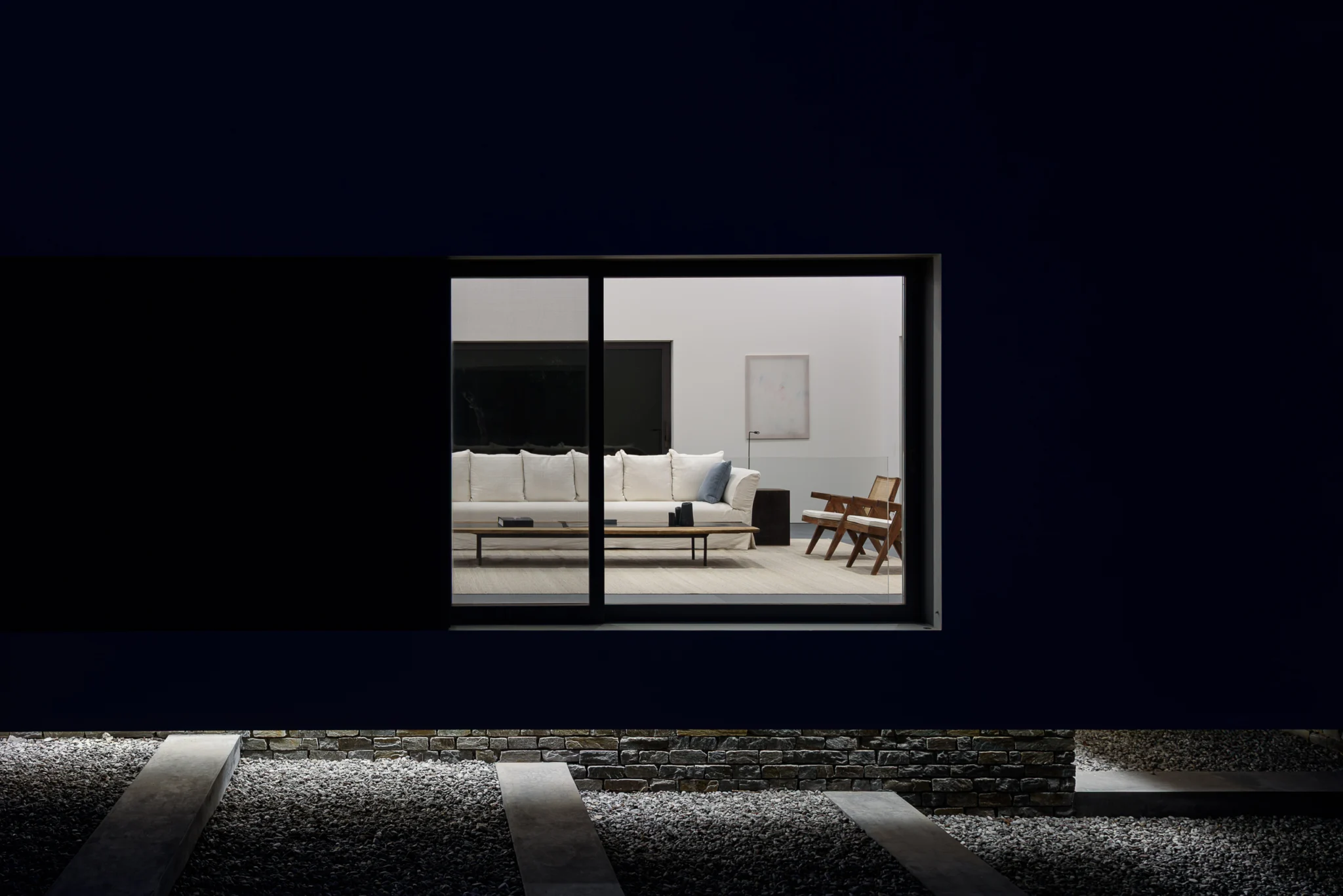 Illuminated living-room window above a stepping-stone path at night at Villa Seafront, Paros.