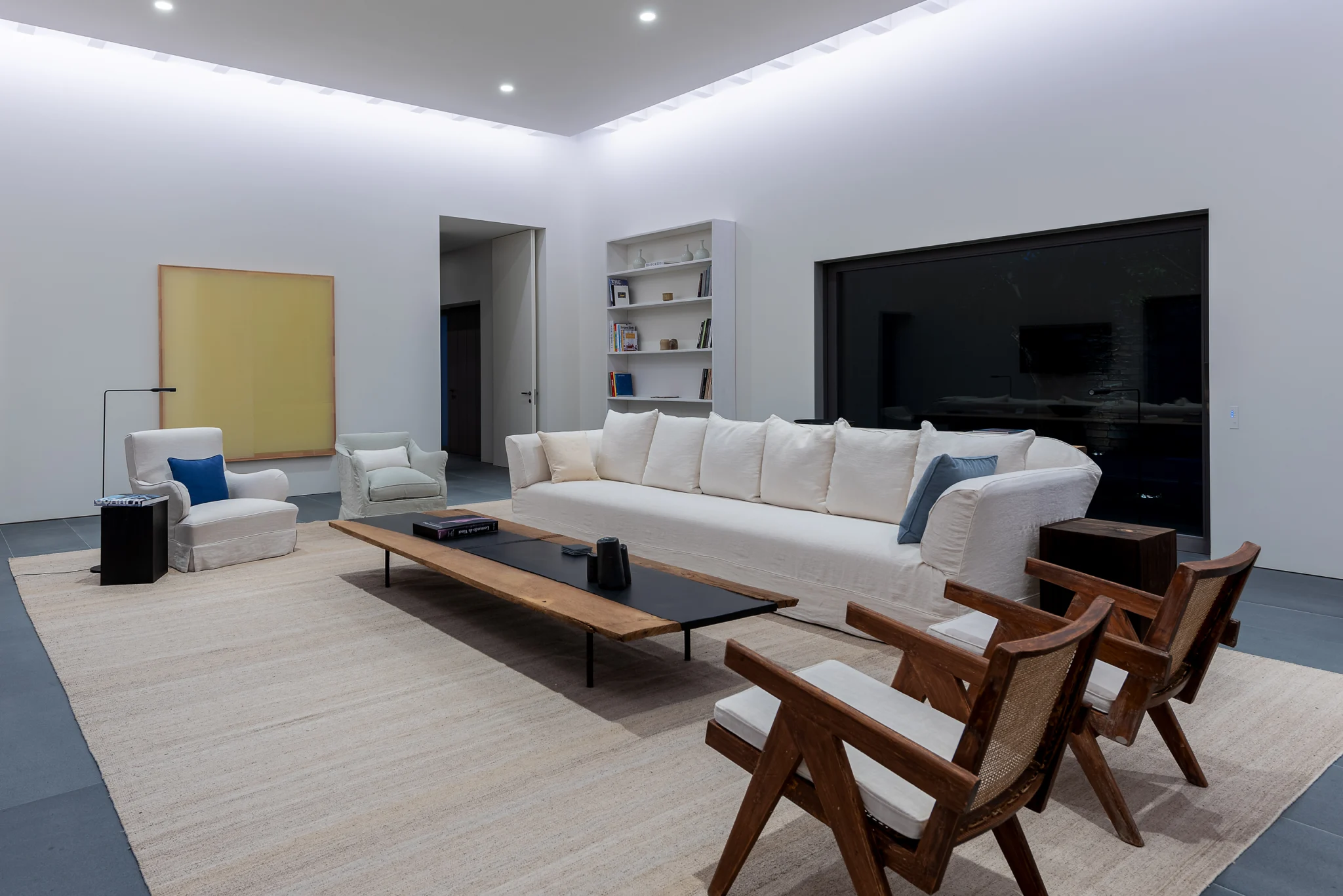 Evening living room with white sofa, timber furniture and yellow artwork at Villa Seafront, Paros.