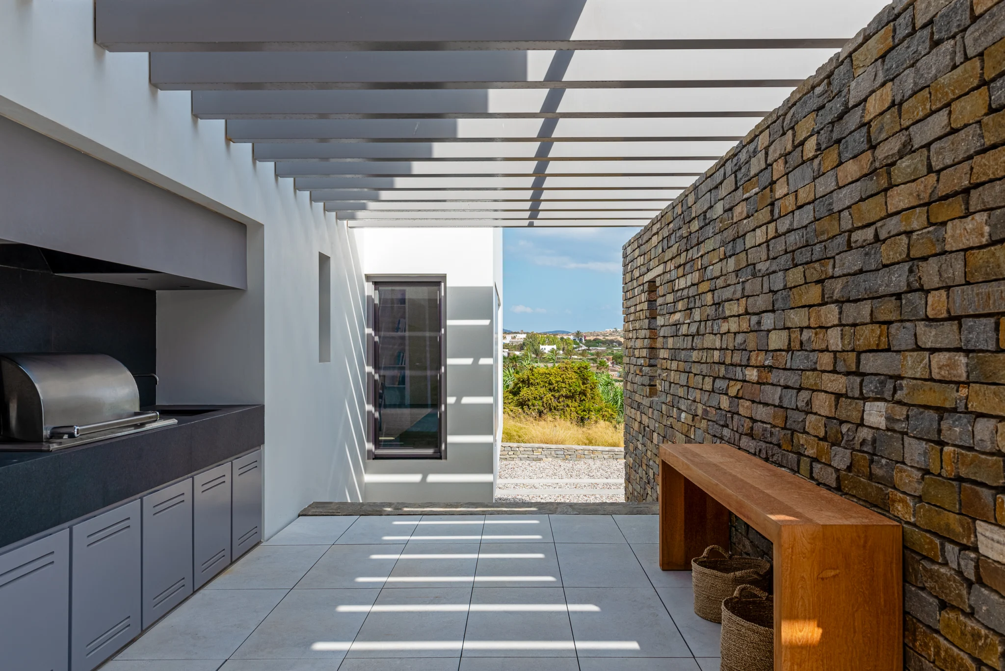 Outdoor kitchen and barbecue beneath a white slatted pergola at Villa Seafront, Paros.