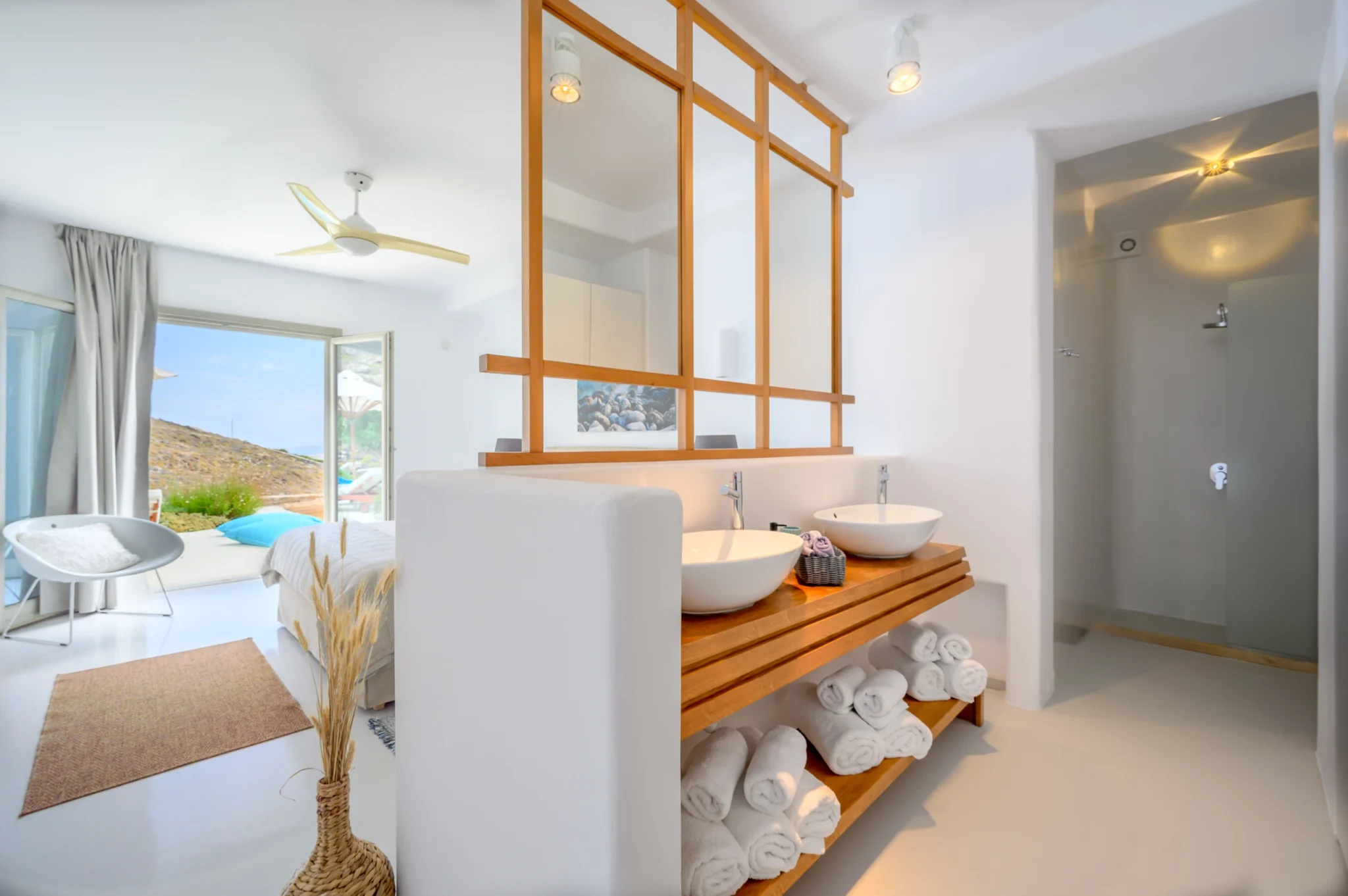 Double vessel basins on a timber vanity beneath a timber-framed mirror partition, with a shower and terrace-facing bedroom at Villa Velvet in Mykonos.