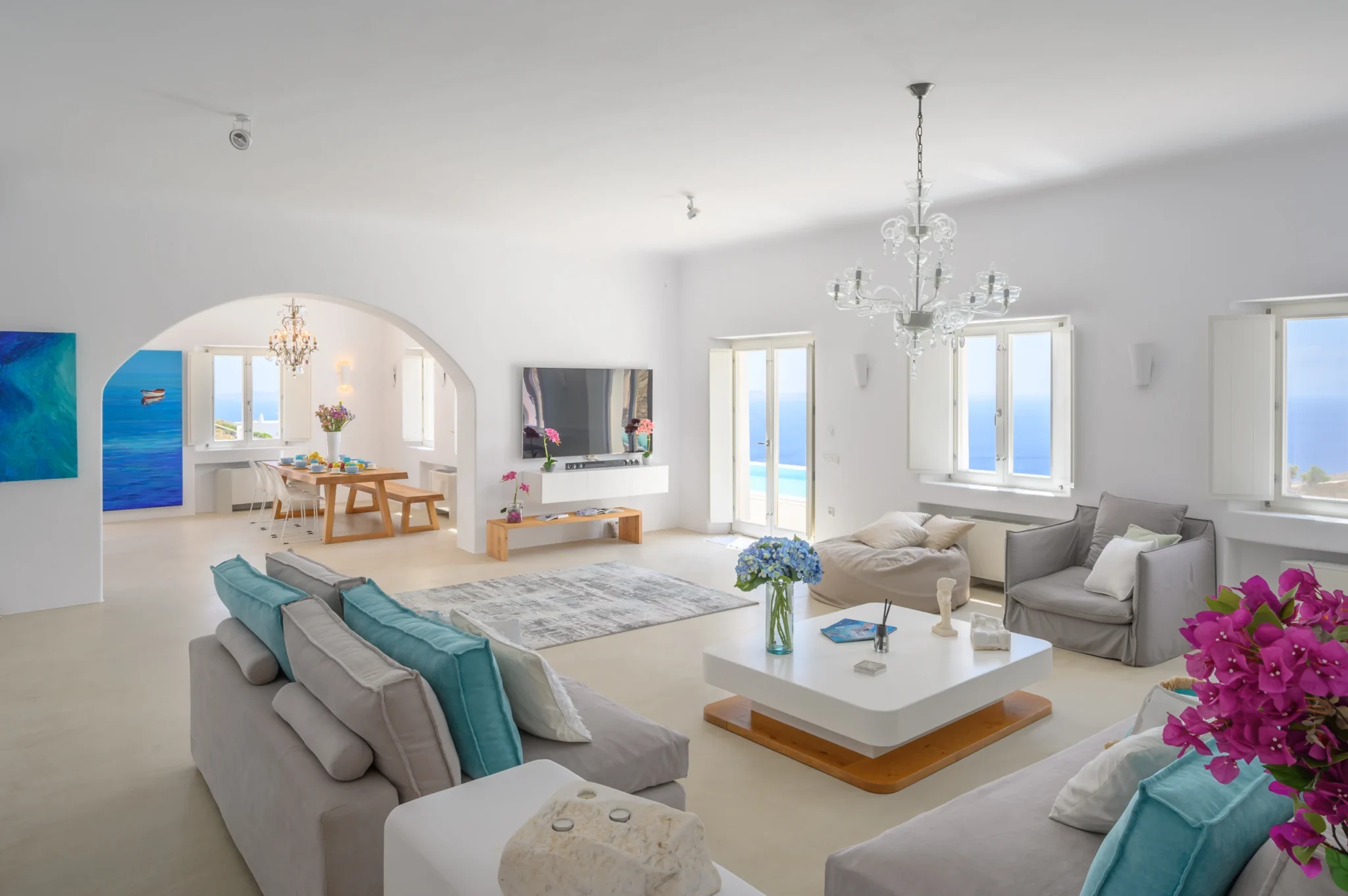 Living room opening through a broad arch to the dining area, with open doors framing the pool and sea at Villa Velvet in Mykonos.