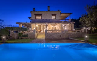 Illuminated stone villa and blue swimming pool at twilight at Villa Vicanti near Pylos, Peloponnese, Greece.