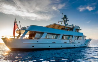 Walanka classic motor yacht on the water in Corfu, with low sunlight reaching around the stern.