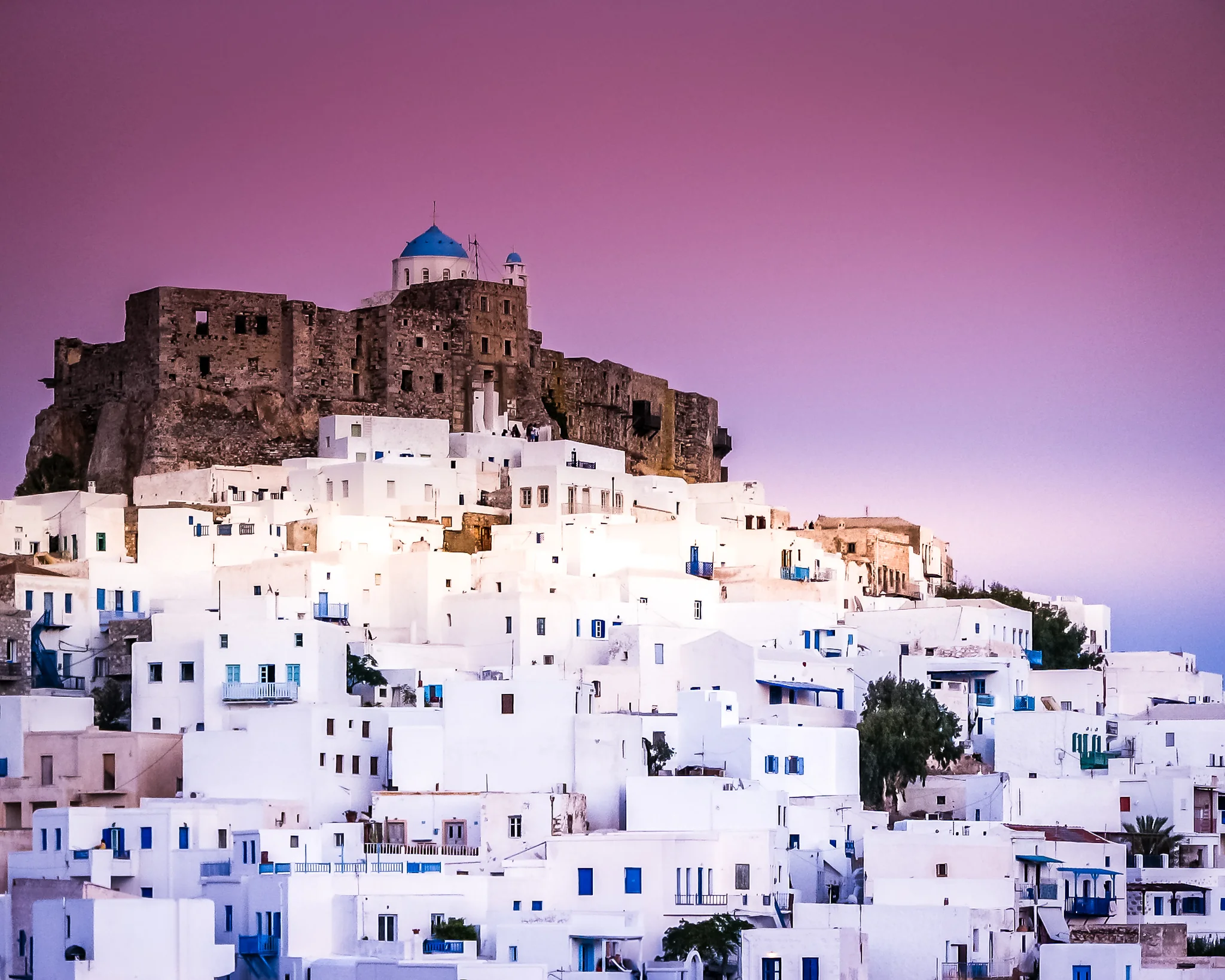 Island Town Beneath the Castle White island town rising toward a stone castle and blue-domed church at dusk
